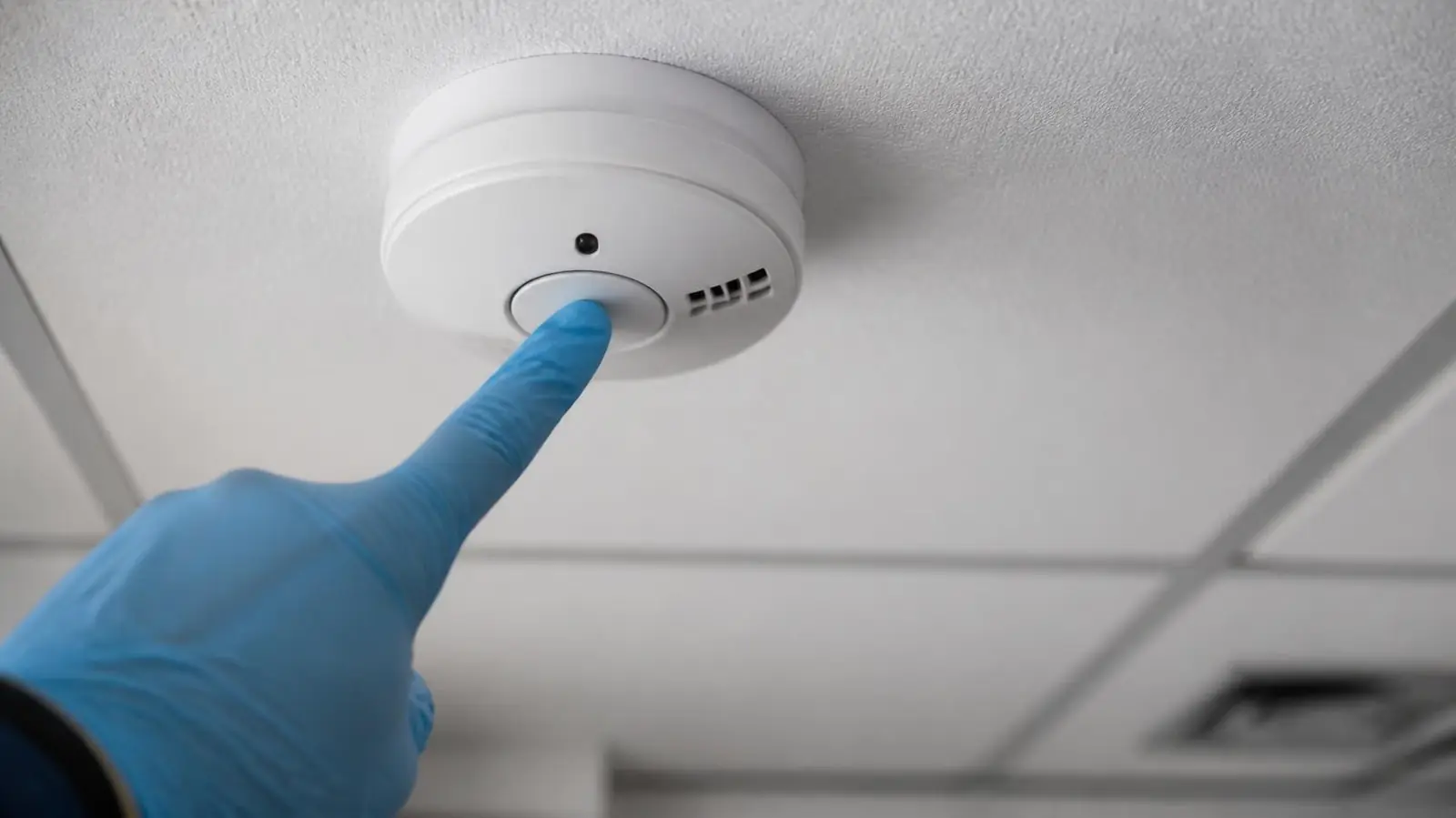 Technician testing a ceiling smoke detector during a commercial fire alarm inspection